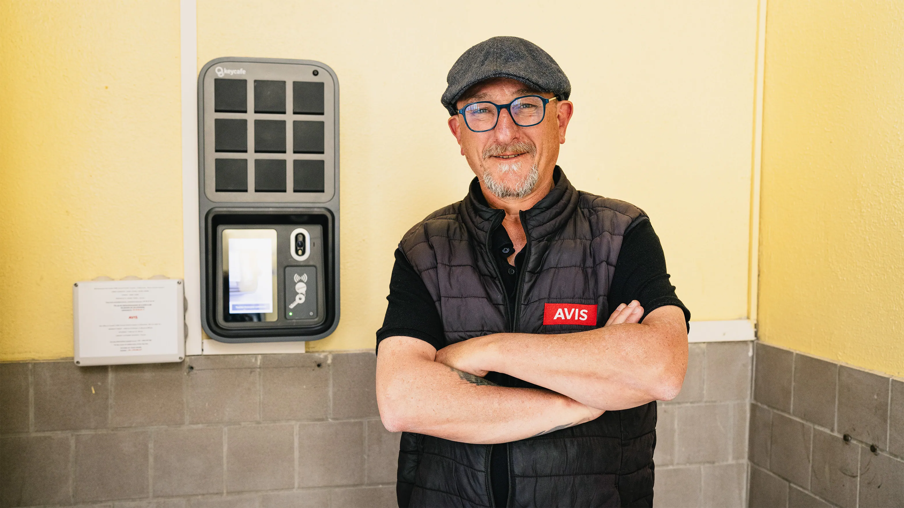 man wearing a Avis Location vest standing in front of a keycafe smartbox