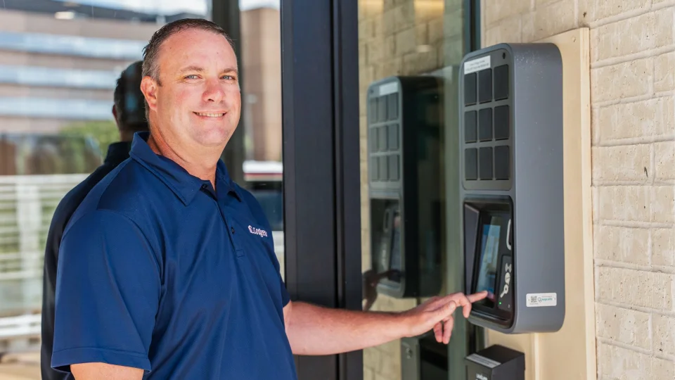 A hotel staff member in a blue polo shirt uses the touchscreen of a wall-mounted Keycafe SmartBox key management system. The automated system allows employees to quickly retrieve or return assigned keys using a unique PIN or badge. Such cloud-connected platforms provide managers with real-time oversight and automated audit trails for every key transaction.