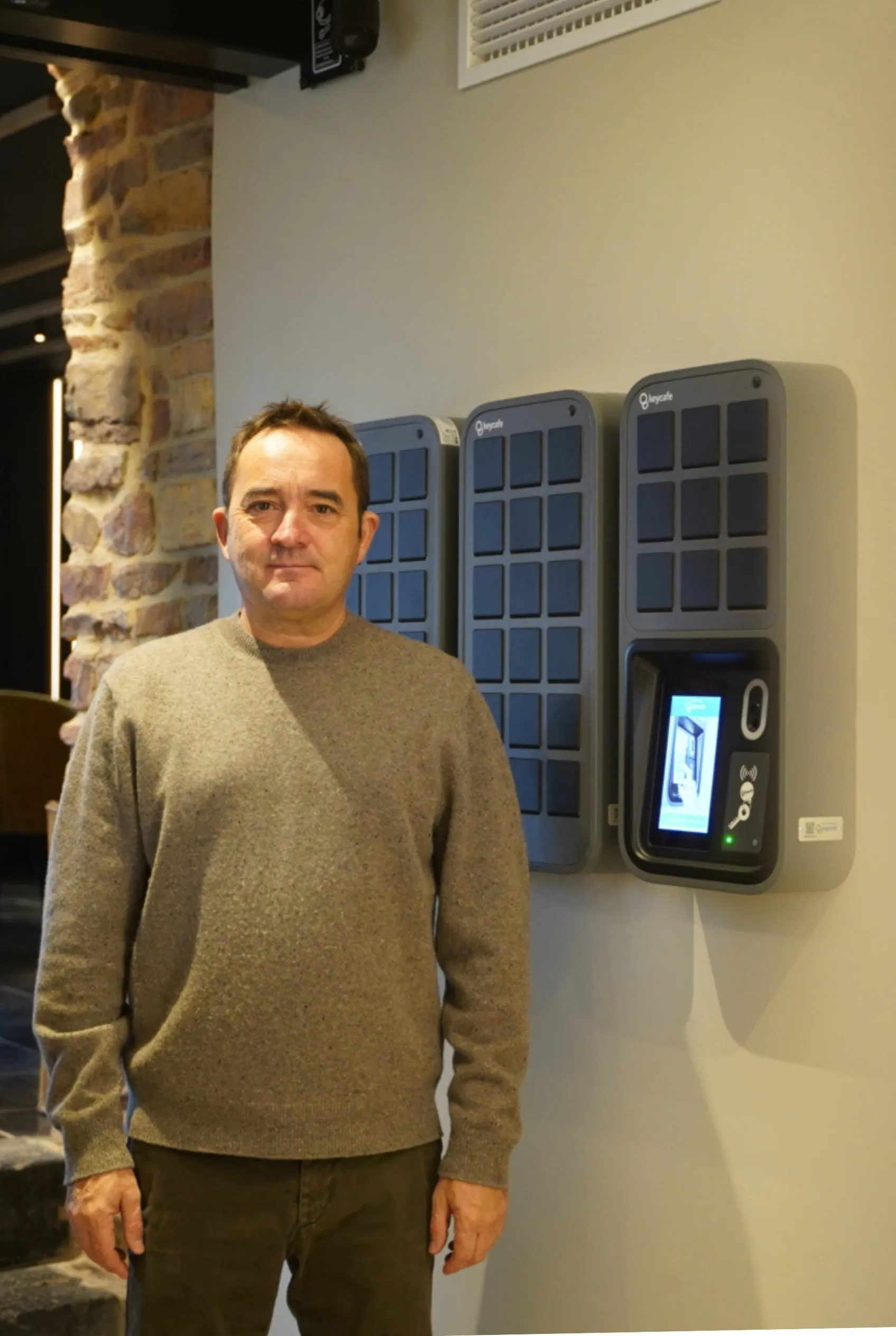 Ein Mann posiert neben modernen elektronischen Schlüsselschließfächern, die an einer Innenwand installiert sind.