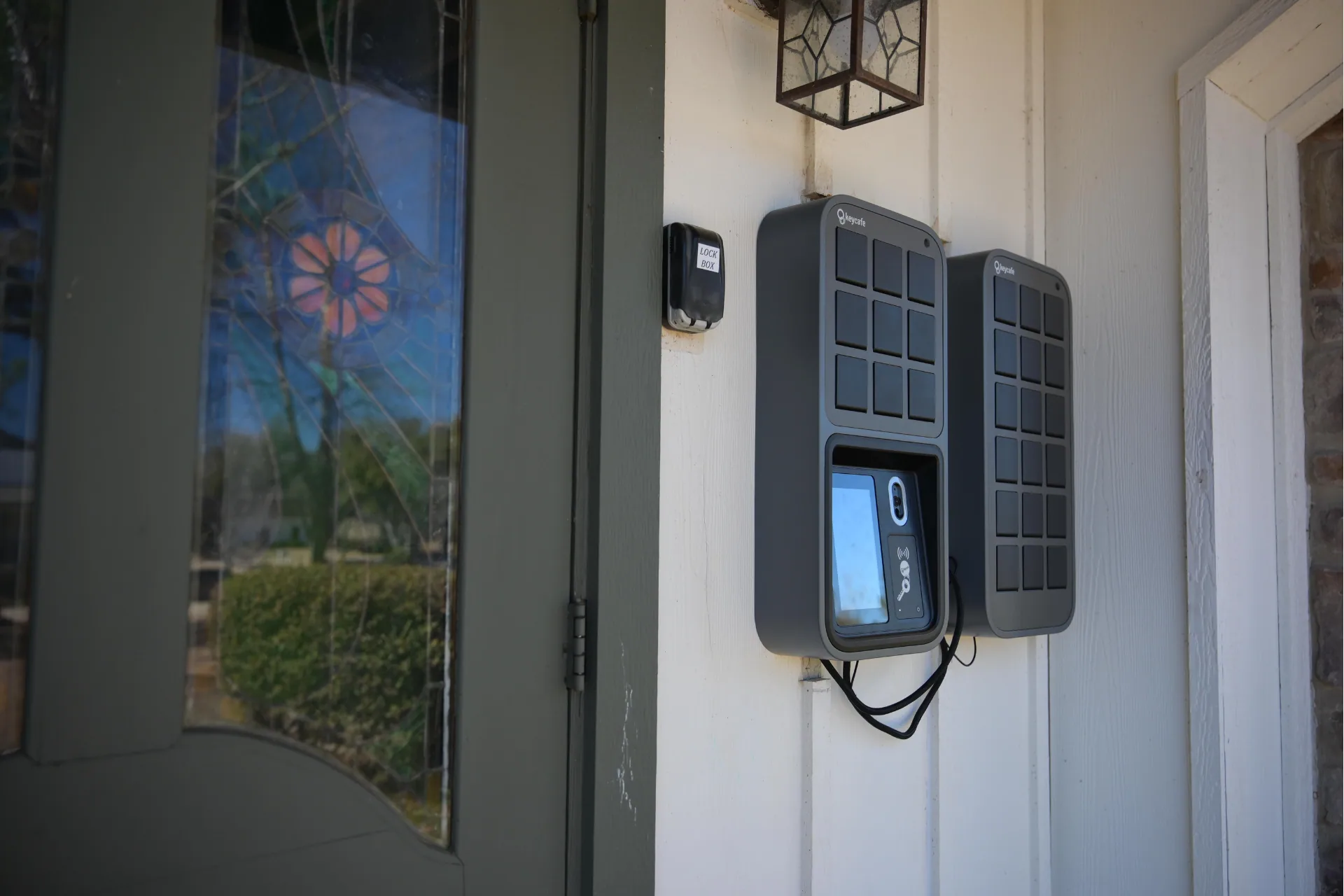 Two Keycafe lockboxes mounted on a white wall next to a green door with a stained-glass window.