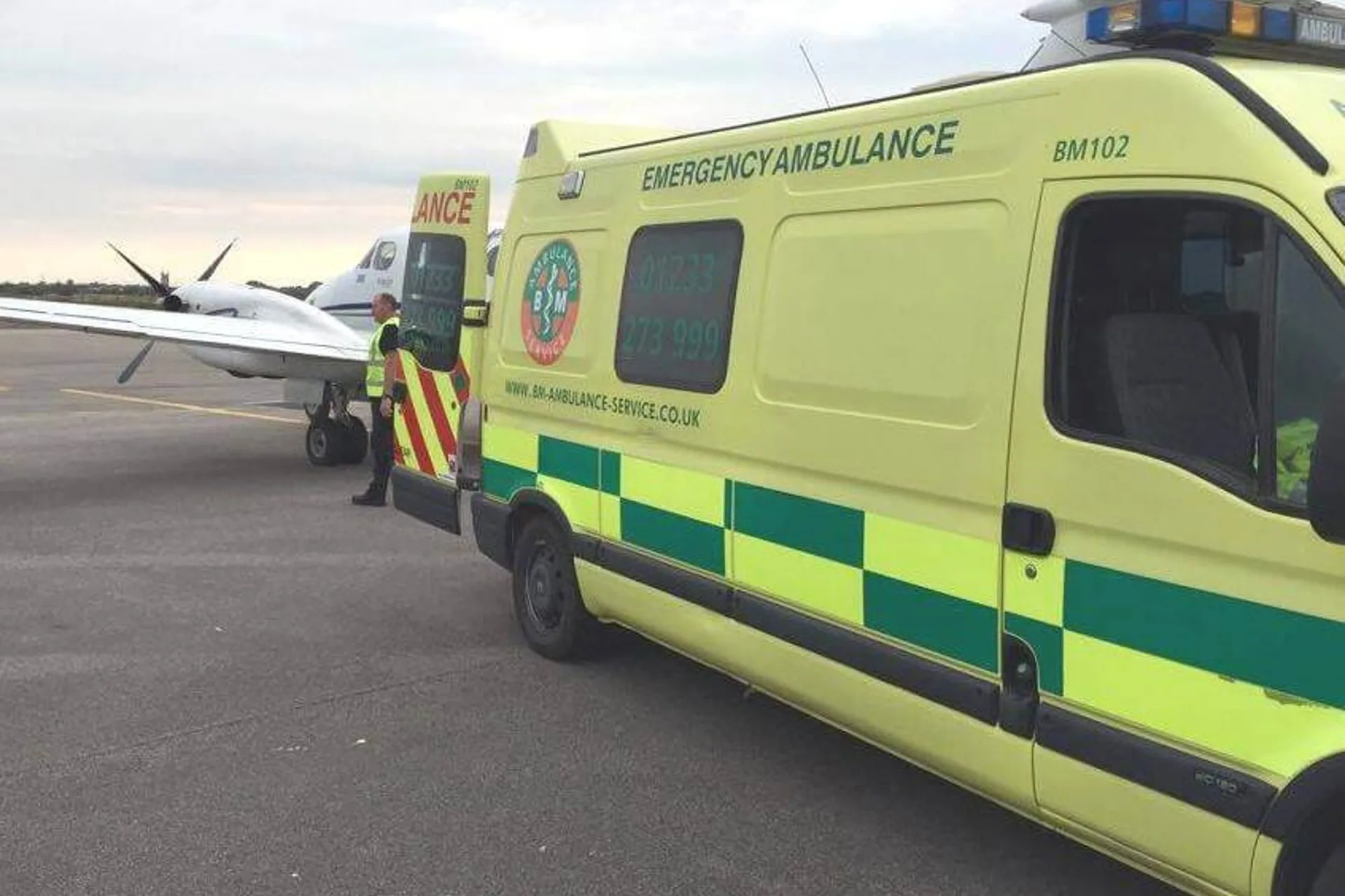 BM-branded ambulance parked at an airstrip beside a plane