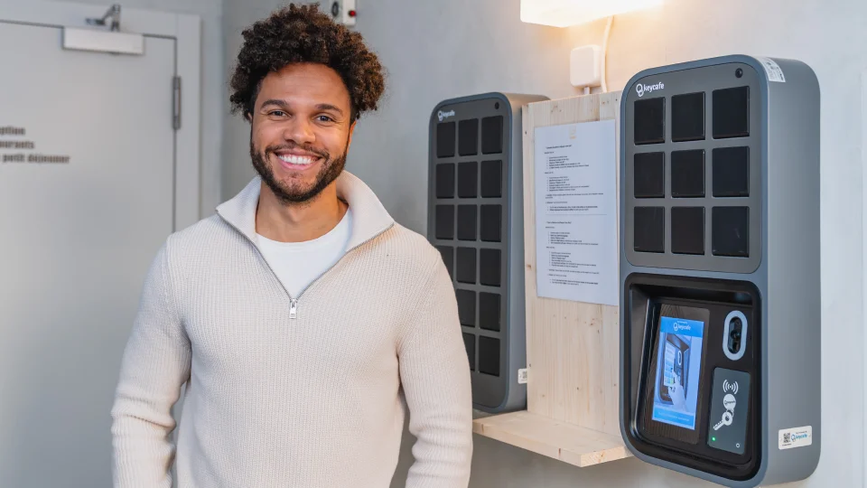 A smiling hotel guest or staff member standing by a Keycafe Smartbox in a hotel lobby, showcasing automated key collection and 24/7 self-service check-in for travelers.