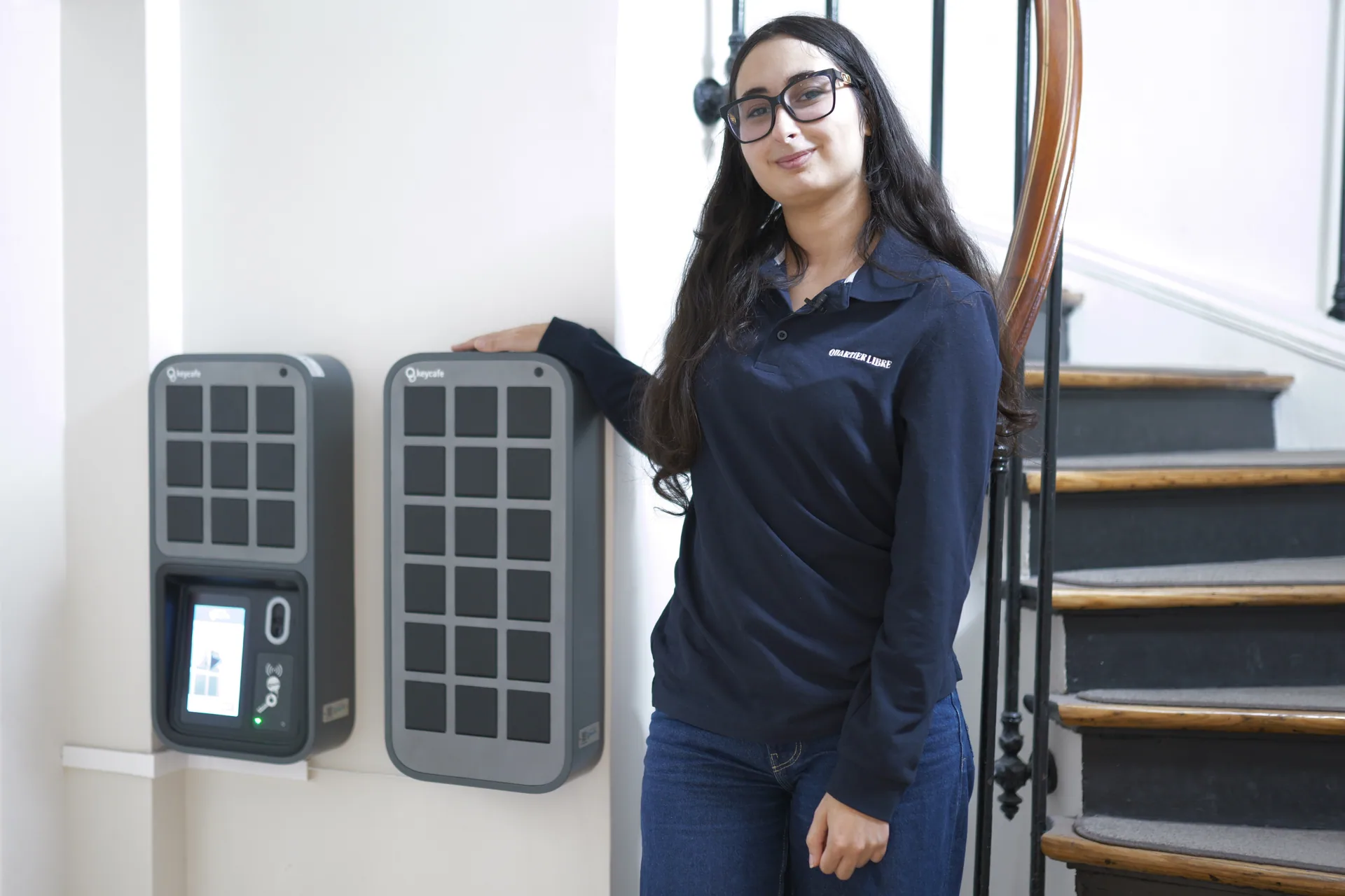 Quartier Libre staff member standing next to Keycafe automated key exchange box in JHMH apart-hotel lobby.