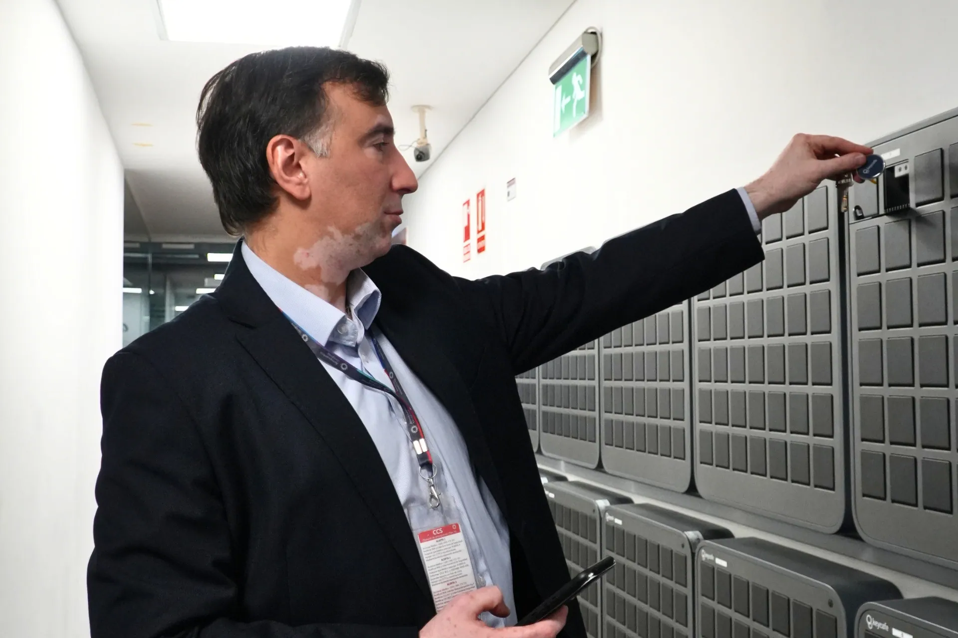 Security Administrative Assistant Gonzalo Moreira using his smartphone to access a wall-mounted Keycafe SmartBox key locker system at Aeropuertos Uruguay