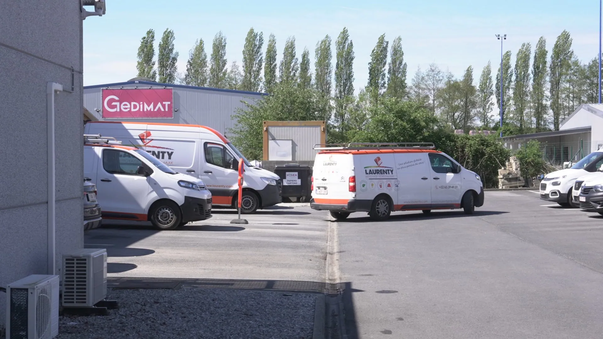 Several white commercial service vans, some branded 'Laurenty', parked in an outdoor lot next to industrial buildings under a clear sky.
