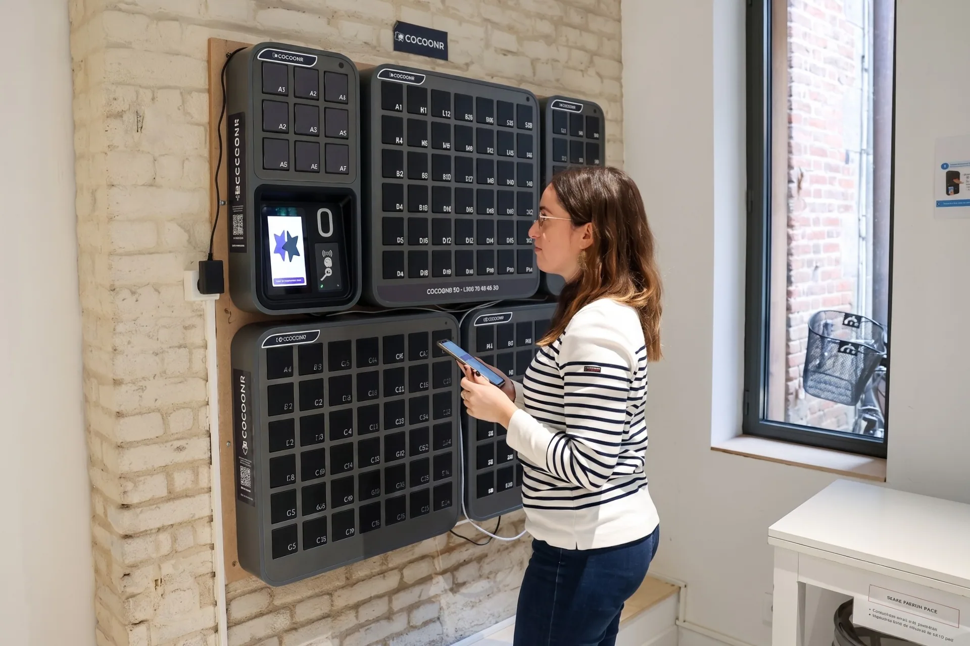 Woman using a digital device next to a wall-mounted smart key box for Cocoonr property management solution