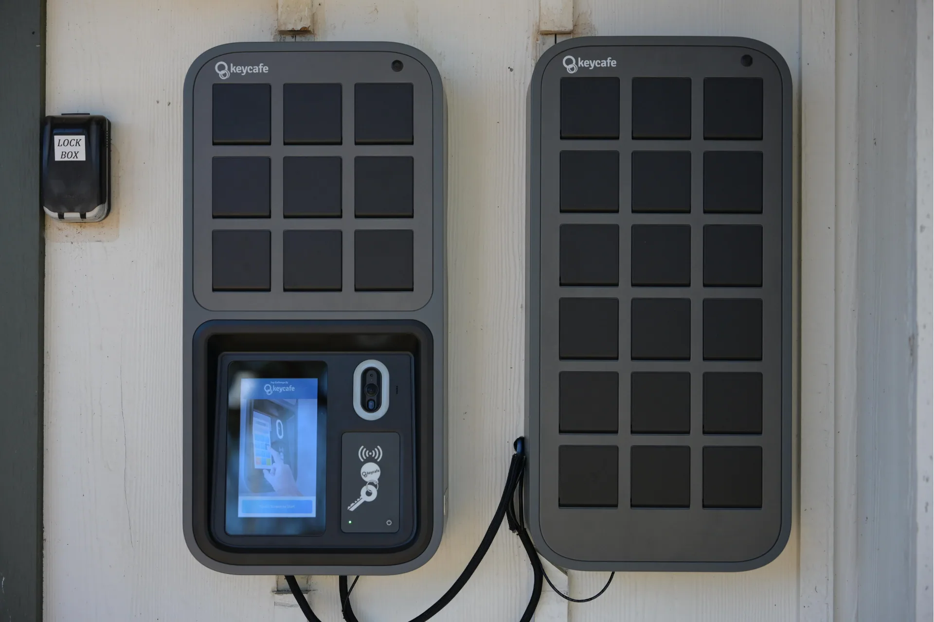 Front-facing view of two Keycafe smart lockboxes mounted side-by-side on a wall.